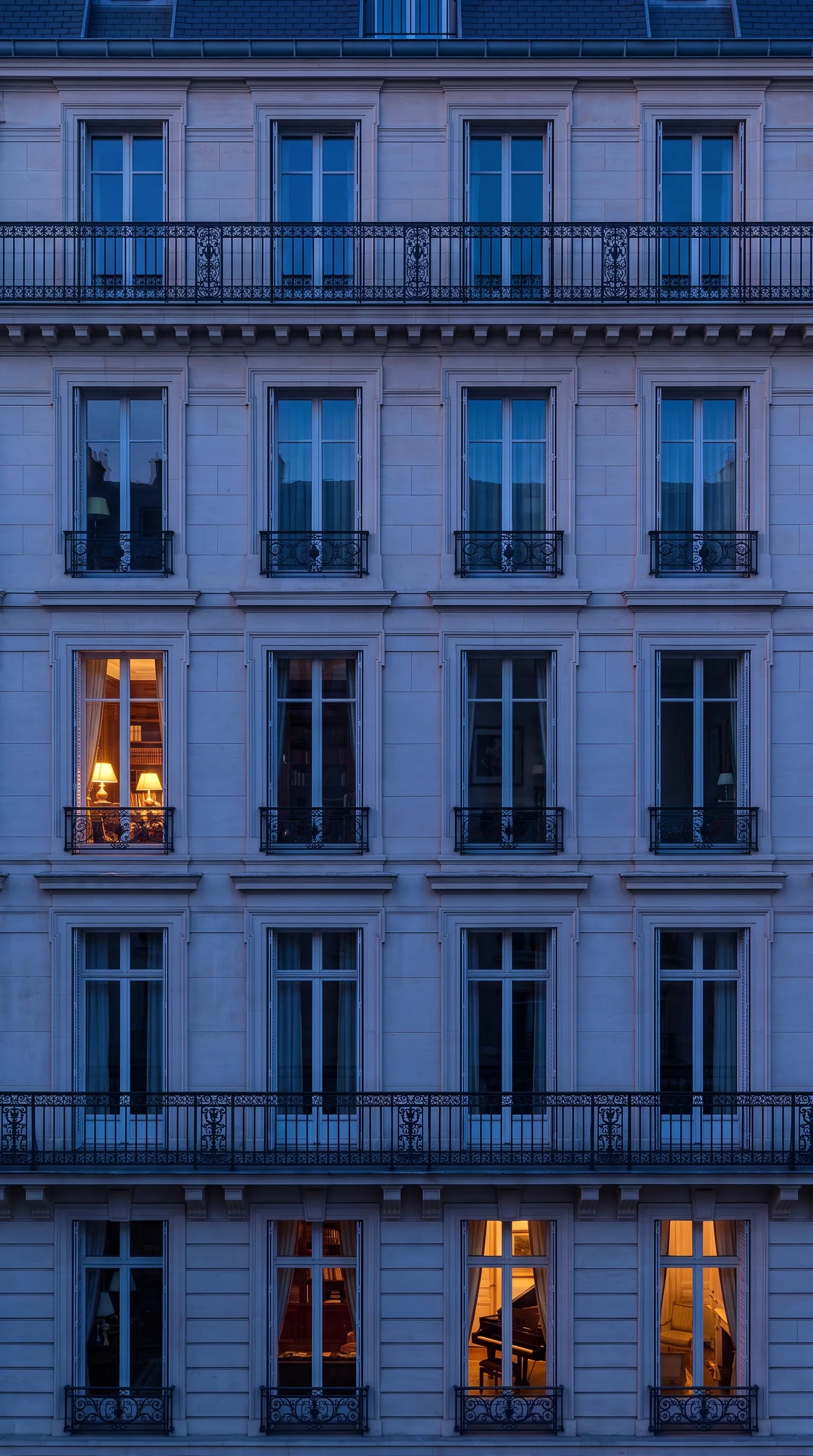 A Parisian stone building at blue hour, its windows lit
